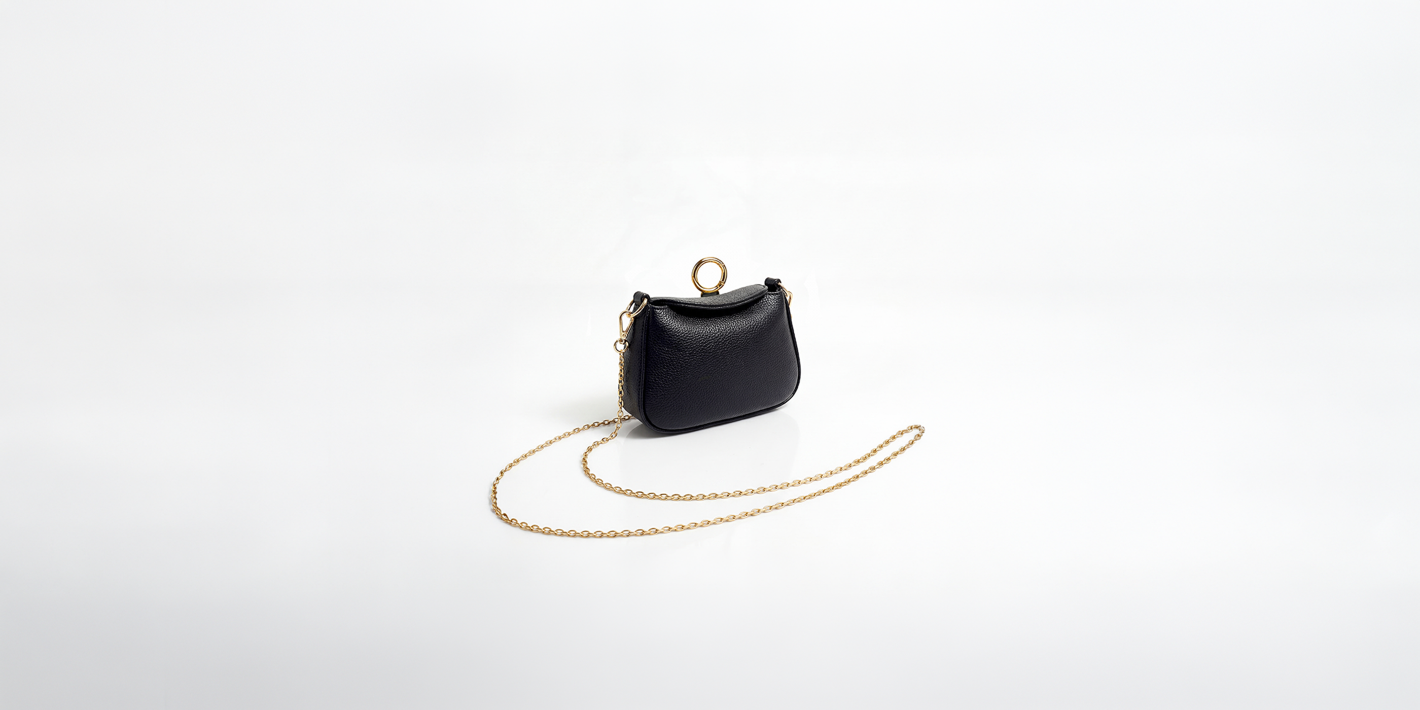 Black NETIC Nano Bag in full-grain Italian leather with chain strap, shown as a compact crossbody bag in an editorial setting